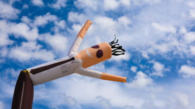 An inflatable tube man, or sky puppet dancer, frolics in the sky over an event in Camarillo, California. The inflatable male figure wears dark sunglasses, a white long-sleeved dress shirt, dark tie and dark dress pants.