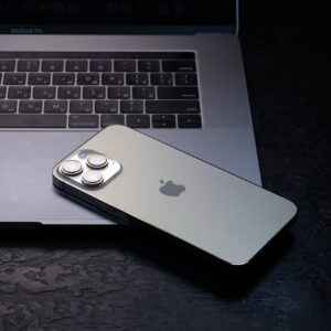 An iPhone is placed face-down on the palm rest of an opened MacBook Pro laptop.
