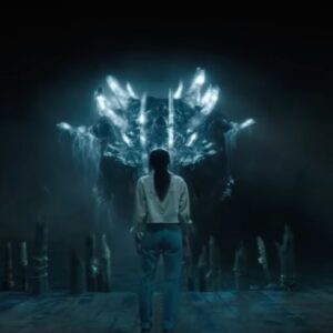 young woman in a dark cave standing with back to camera facing a gigantic monster glowing blue