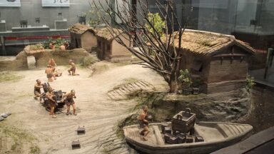 photo of a diaorama showing a Bronze Age cillage, with people pulling something on a sledge toward a boat