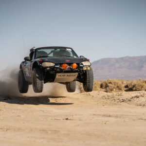 An off-road modified Miata gets some air as it drives off-road.