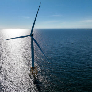 A aerial view of a large, sunlit expanse of ocean with a single wind turbine in it.