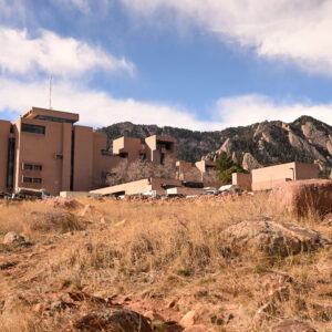 The National Center for Atmospheric Research in Boulder, Colorado on December 17, 2025. Clay colored building with grass and red rocks in foreground.