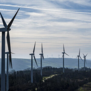 Dry, shrub colored hillsides with a large series of wind turbines poking up into a sky filled with wispy clouds.