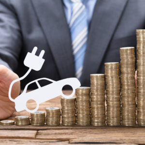 Midsection of businessman protecting coins with electric car at wooden table