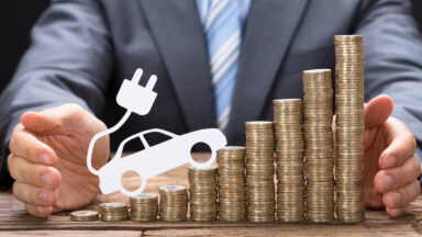 Midsection of businessman protecting coins with electric car at wooden table
