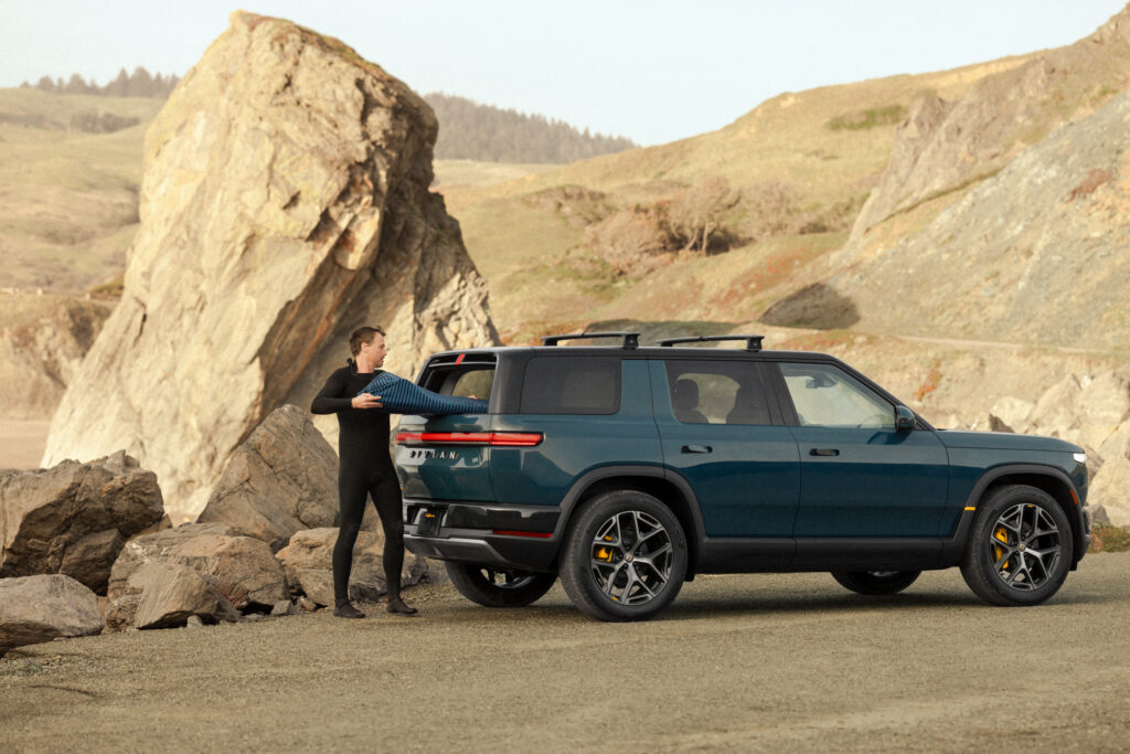 A man puts a surfboard into the back of a Rivian R2
