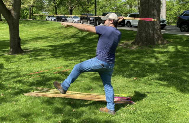 Bearded man, side view, with one leg lifted and a javelin attached to a spear-thrower held in one hand, arm raised to shoulder height, poised to throw it