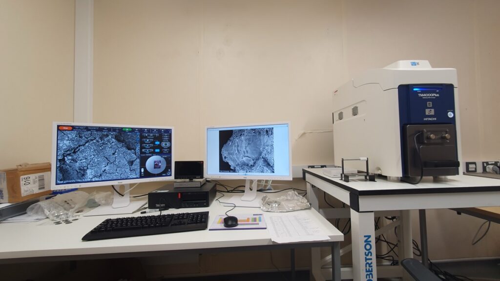 lab desk with three computer monitors showing archaeological samples on the screens