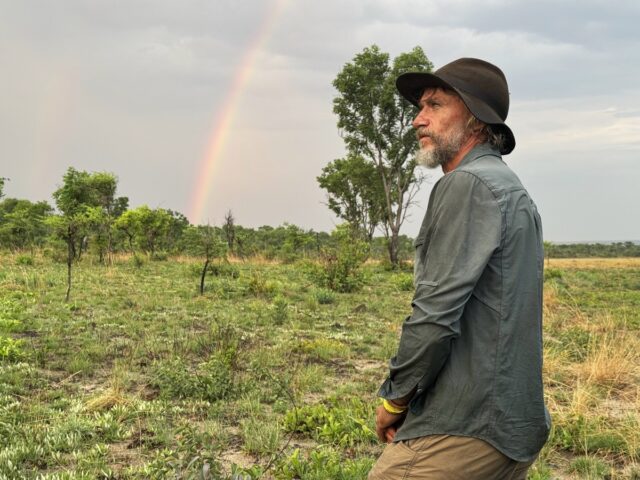 Dr. Steve Boyes, with a rainbow in the background, experiences the first signs of the rainy season.