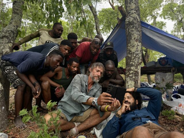 A group of Angolan tribal hunters, Dr. Steve Boyes, and Kerllen Costa, check Steve's cellphone video of a ghost elephant.