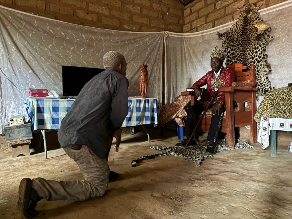 Xui kneels in front of the local king, Regedor Kaketche, during an audience granted for the expedition. The king sits on his leopard throne.