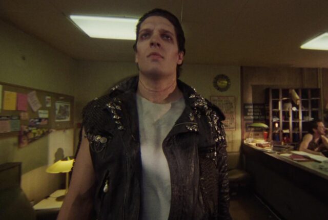 Large dark haired man in leather vest and white tee shirt and multiple piercings