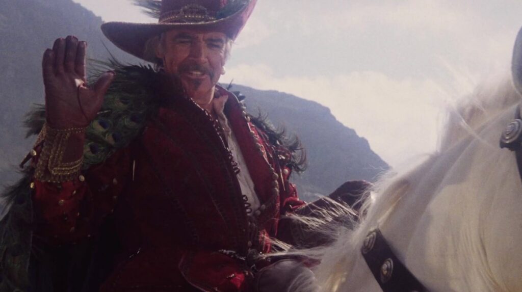 Middle aged man with silver hair and beard on a white horse, wearing a flamboyant Spanish conquistador costume