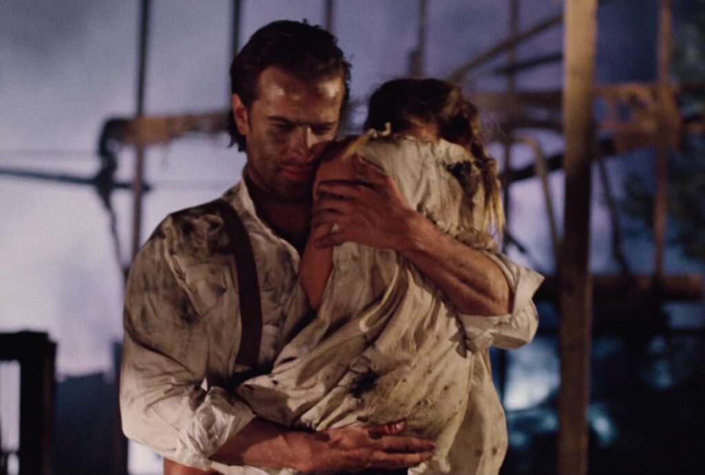 man in 1940s garb in a war zone carrying a little girl out of a bombed-out wreckage