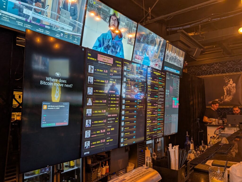 Image of a bar showing multiple large, flat screen TVs behind it showing some decidedly atypical viewing, such as bitcoin futures.