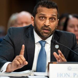 FBI Director Kash Patel sits at a table and speaks into a microphone while gesturing with his hands.