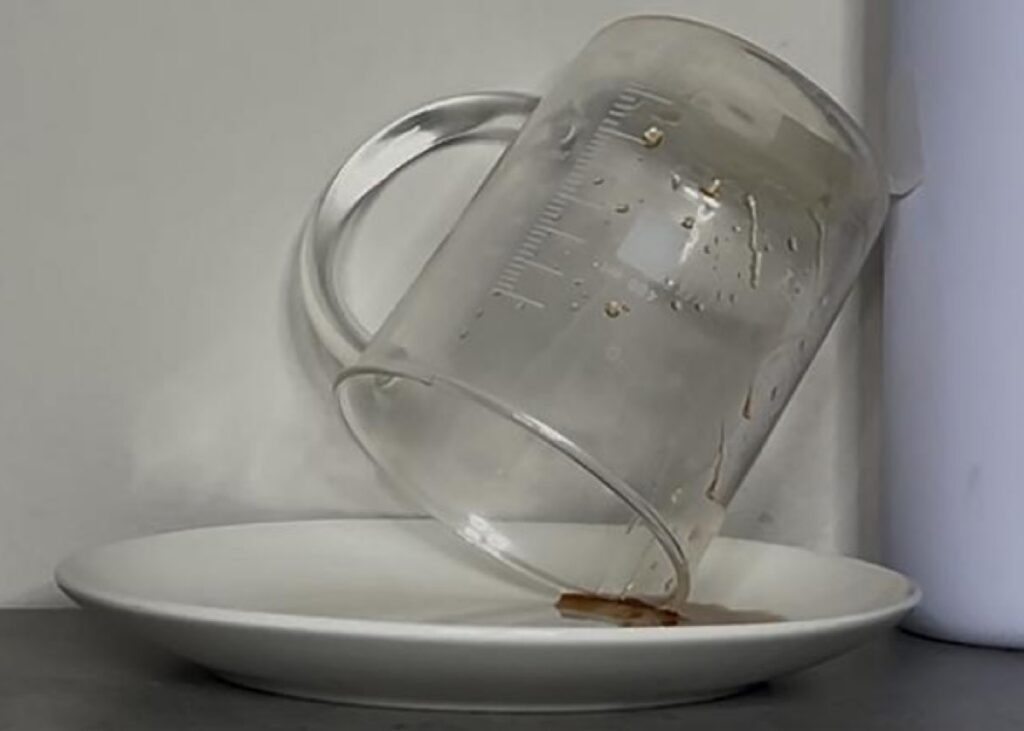 measuring cup tipped over on side on top of plate as last dregs of olive oil drip out