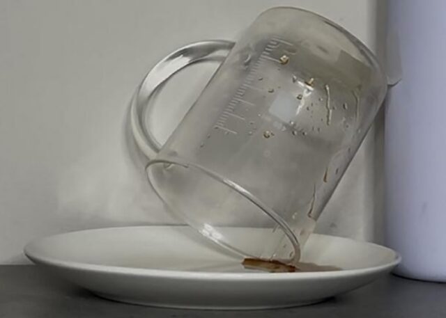 measuring cup tipped over on side on top of plate as last dregs of olive oil drip out