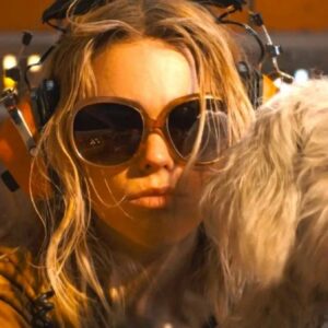 young blonde woman wearing sunglasses and pouting at the camera with a fluffy white dog next to her