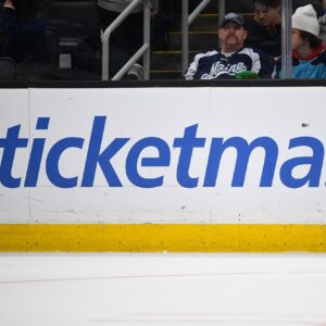 A large Ticketmaster logo on the boards inside an ice hockey arena.