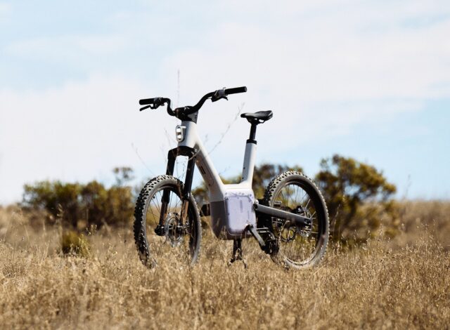 A field with high grass, and a bicycle sitting in the middle of it. The bicycle has a distinctive square assembly in the region where the cranks are located on a normal bicycle.