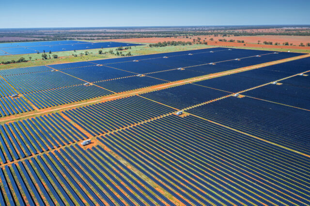 image of a red, dusty scrubland covered in row after row of photovoltaic panels.