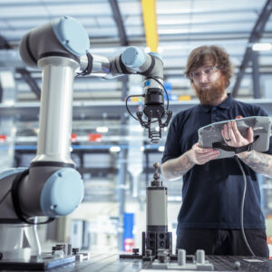 Image of a man with a computer tablet standing in front of an industrial robotic arm.