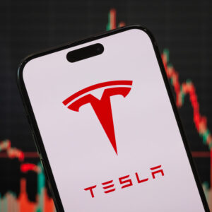 CHONGQING, CHINA - APRIL 20: In this photo illustration, the Tesla logo is displayed on a smartphone screen, with the company's stock market performance and candlestick chart visible in the background, highlighting Tesla's financial movements and its prominent role in the electric vehicle, renewable energy, and autonomous driving sectors, on April 20, 2025, in Chongqing, China. (Photo illustration by Cheng Xin/Getty Images)