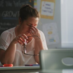 Tired Female Teacher Sitting Alone at the Desk in Empty Classroom. Woman Feeling Stress, Burnout and Mental Exhaustion in Educational Environment, Working in Elementary School.