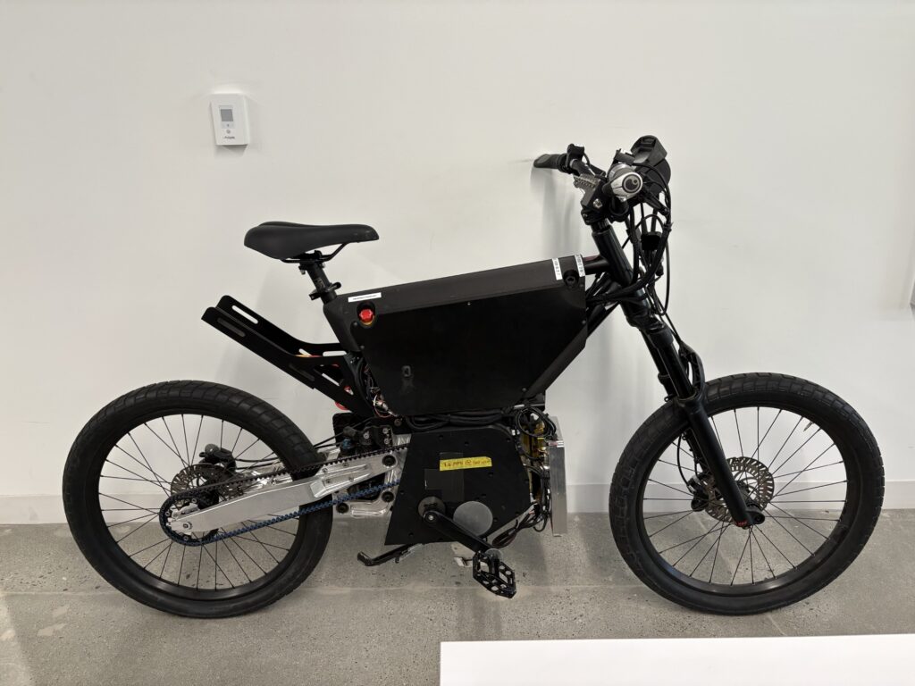 Image of a black bicycle, with a lot of exposed hardware suggesting it is unfinished.