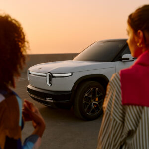 A white Rivian R2 with two women standing in front of it