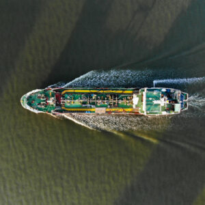 A top-down aerial view of a tanker ship churning through the water with a visible wake. Oil tankers and gas tankers were affected by the closure of the Strait of Hormuz, leading to a global energy crisis stemming from the war in the Middle East.