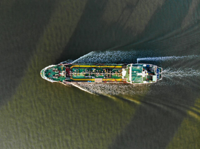 A top-down aerial view of a tanker ship churning through the water with a visible wake. Oil tankers and gas tankers were affected by the closure of the Strait of Hormuz, leading to a global energy crisis stemming from the war in the Middle East.