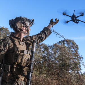 Wearing a camouflaged uniform and helmet, Marine Corps Cpl. Calvin Burke holds his arm outstretched as he activates a small drone to survey the defensive line for opposing forces during a simulated assault and seizure at Glen Airfield, Queensland, Australia, July 2025.