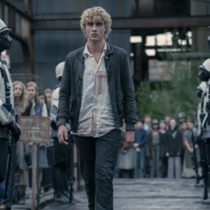 young man with tousled blonde hair walking between two rows of potential tributes