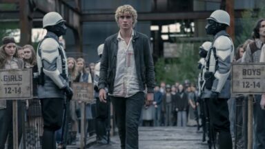 young man with tousled blonde hair walking between two rows of potential tributes