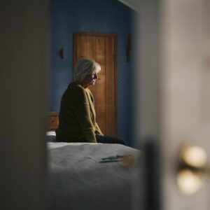Sad elderly woman sitting on bed in bedroom at home