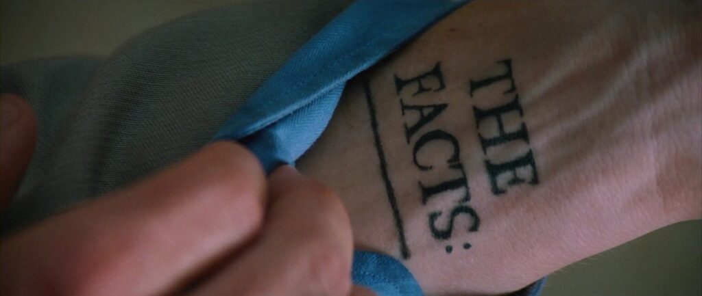 closeup of a hand turning down a sleeve to reveal a tattoo reading "The facts."