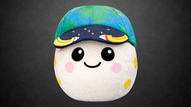a plush moon with pink and yellow craters, two eyes and a smile, wearing a blue and green cap