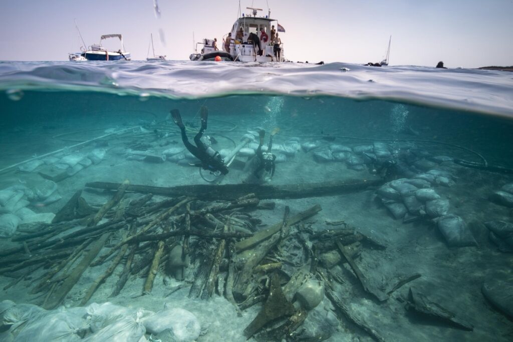 View of the excavation of the bow area of the Ilovik-Paržine 1 shipwreck. In the foreground, the cargo of logs and amphoras can be seen. Archaeologists are working near the structure of the bow complex.