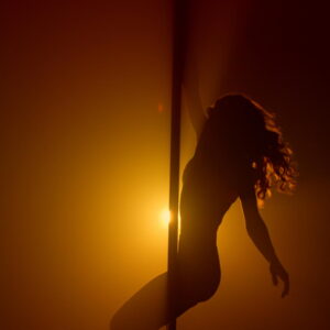 Flexible woman silhouette practicing poledance in nightclub spotlight. Sexual lady turning round pole making acrobatic tricks. Sensual girl pole dancing sexually in soft backlight
