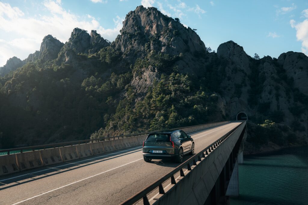 A Volvo EX60 drives away from the camera over a bridge.