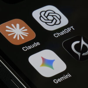 An iPhone screen photographed at close range displays four AI assistant application icons, including Claude by Anthropic, ChatGPT by OpenAI, Gemini by Google, and Grok by xAI.