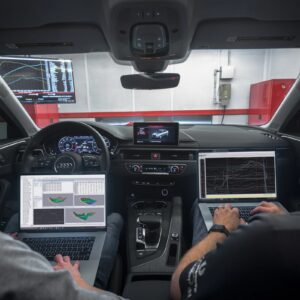 Two men with laptops sit in the front seats of a car