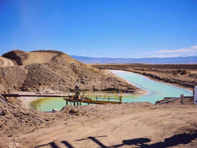 Image of a dry, plant less desert area. In amidst large lumps of soil sit a human-shaped pond of vivid blue water.