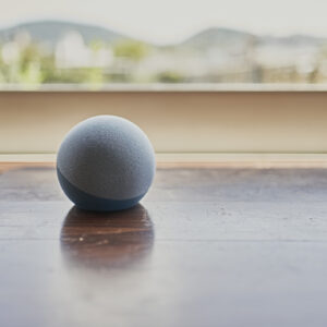 An Amazon Echo Dot smart speaker on a table by a window.