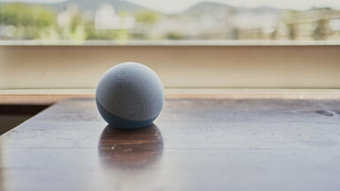 An Amazon Echo Dot smart speaker on a table by a window.