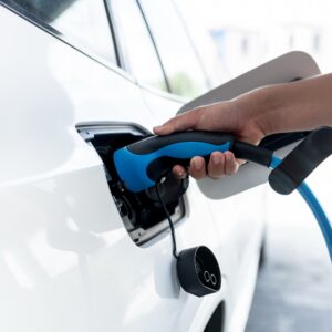 A parking lot with charging stations for electric cars. A hand holds a charging handle while charging an electric car at a home charging station.
