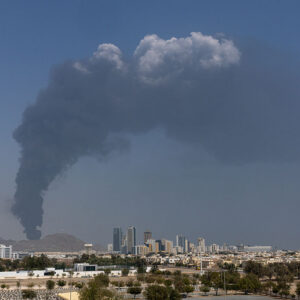 Photo shows the city landscape of Fujairah, United Arab Emirates in the foreground with high-rise buildings and other buildings, while a black tower of smoke rises in the background beyond some hills after an explosion in the industrial zone caused by debris after interception of an Iranian drone by air defense on March 5, 2026.